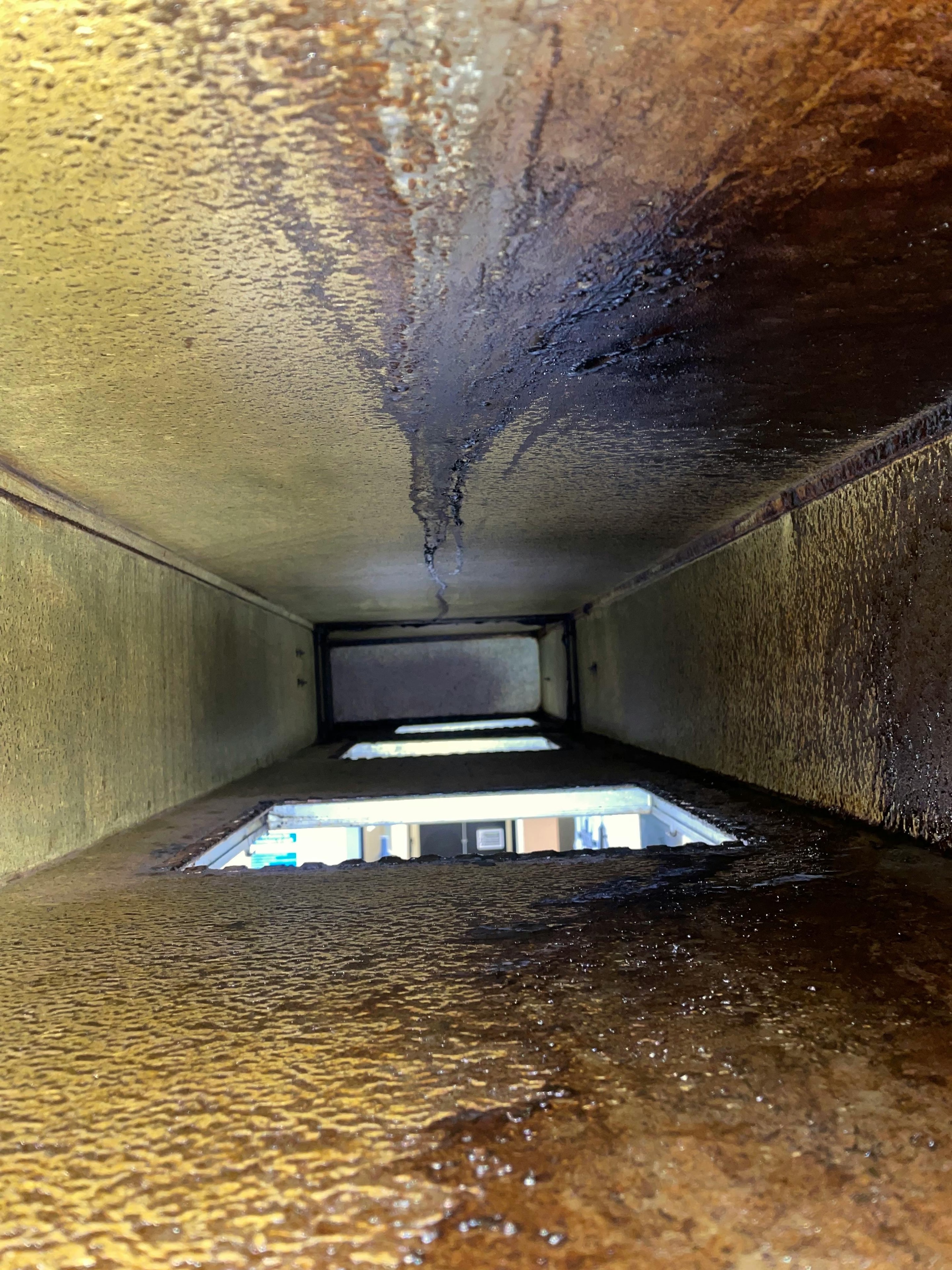 Inside view of commercial kitchen ductwork before TR19 cleaning — heavy grease and carbon build-up coating all surfaces